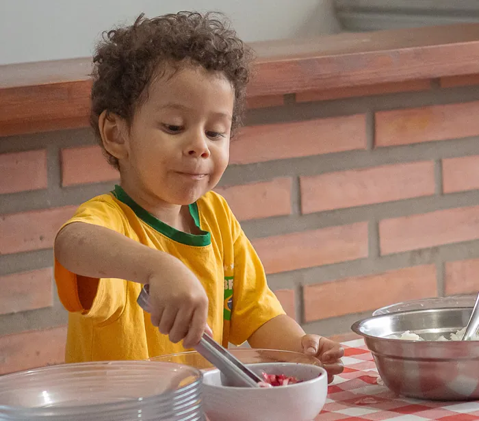 Criança servindo comida com uma pinça durante o almoço na escola